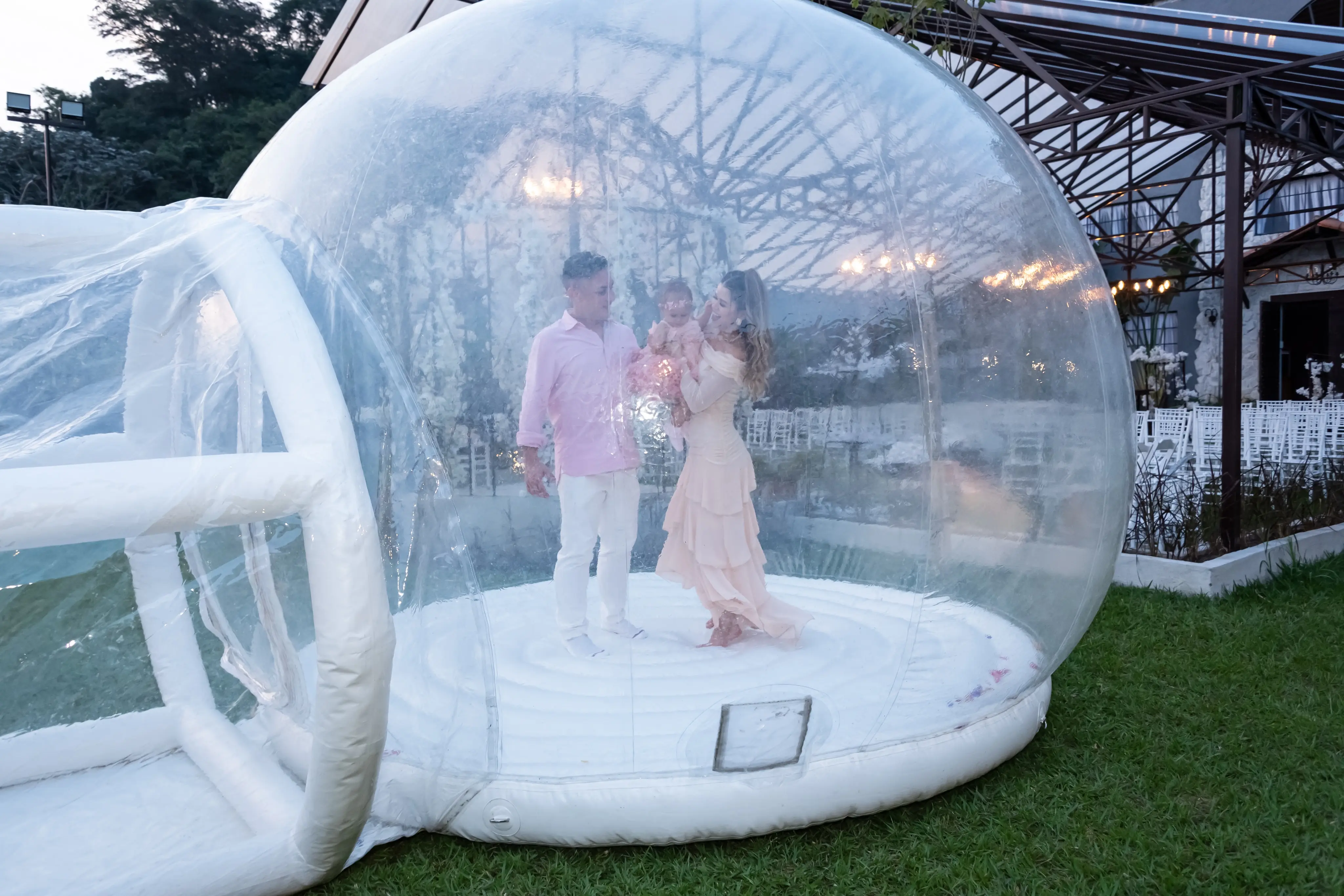 Casal com a filha no colo dentro de uma tenda-bolha transparente montada no gramado