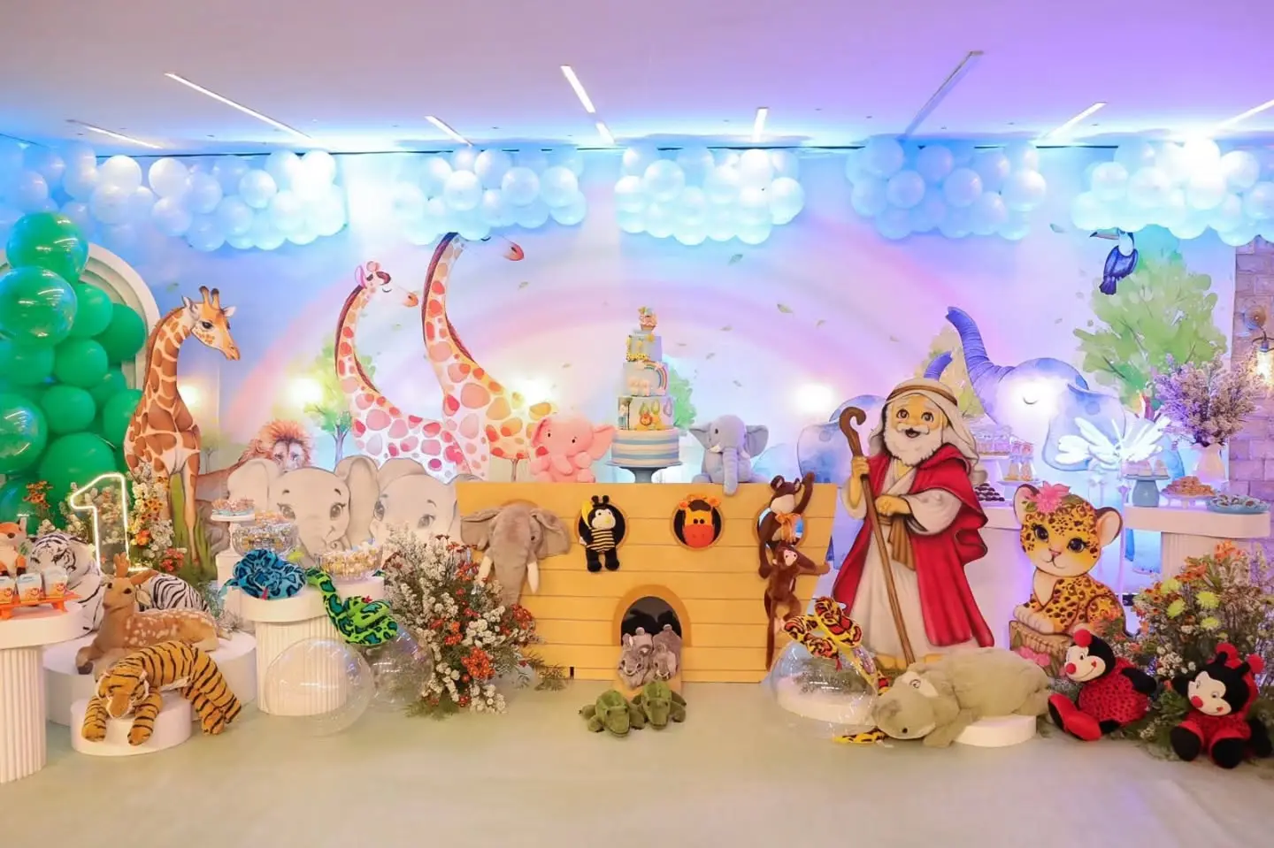 Mesa de festa infantil com tema de animais da floresta: girafas, leões, macacos e balões em tons pastel